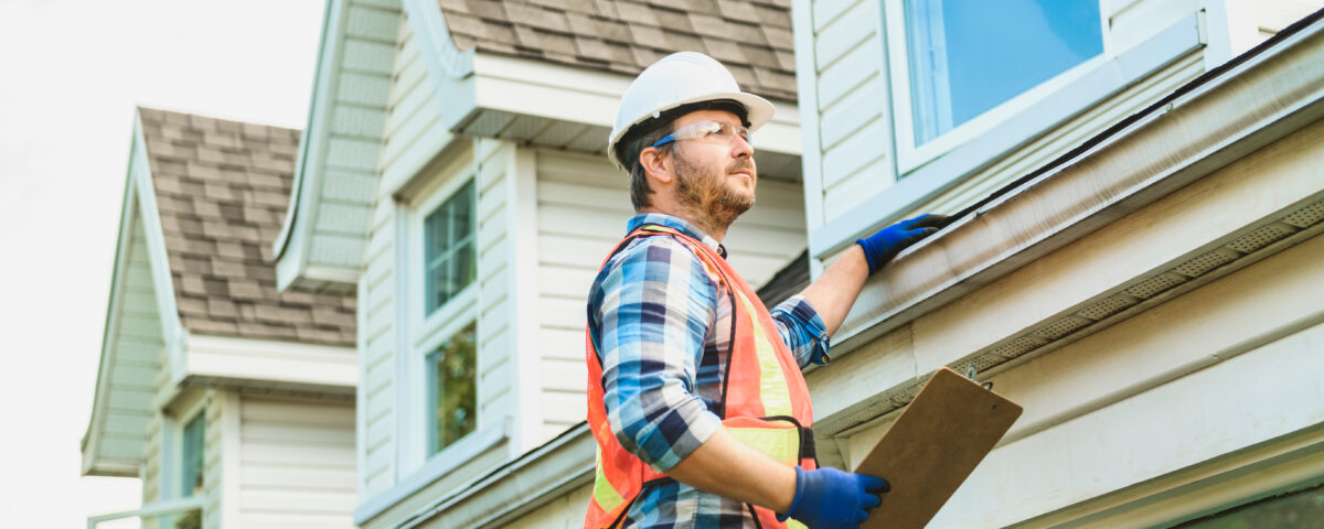 man with hard hat standing on steps inspecting house roof